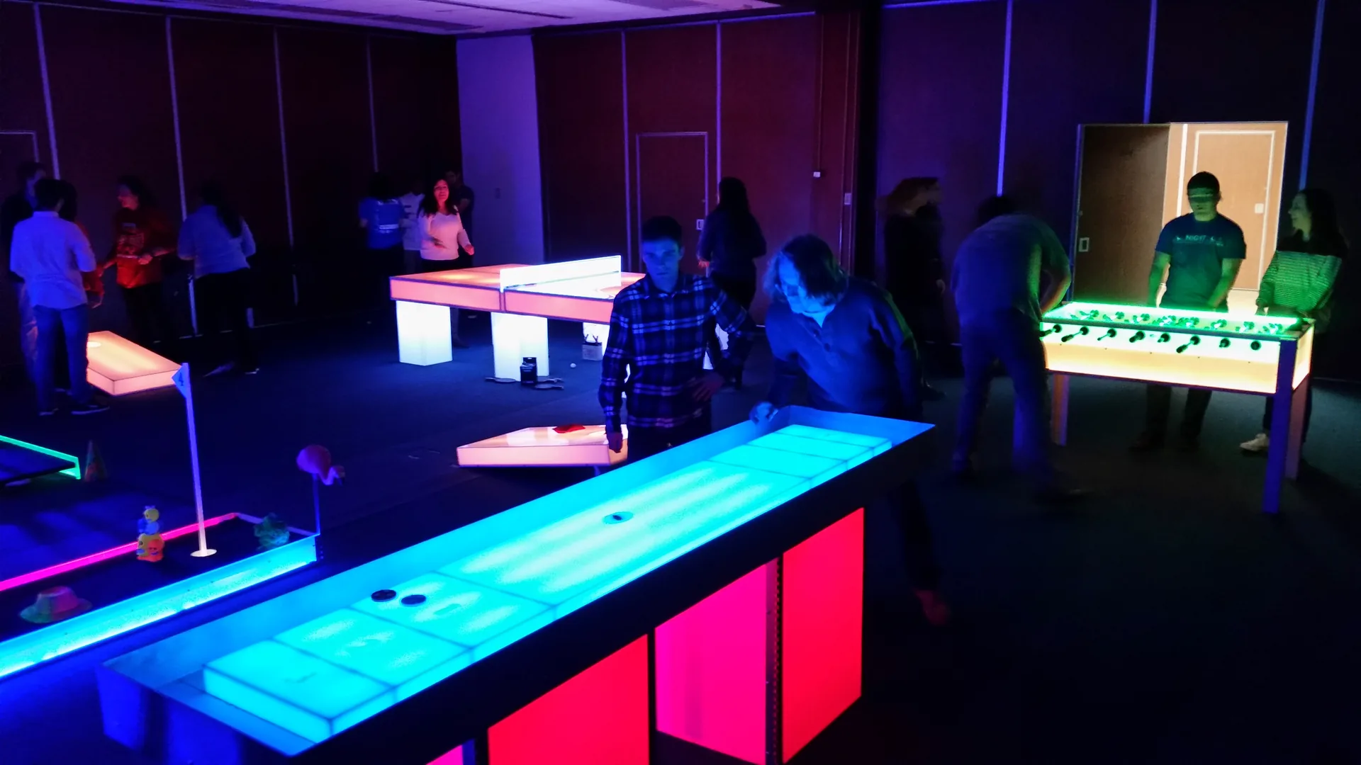 Guests playing glow shuffleboard and foosball at an evening event