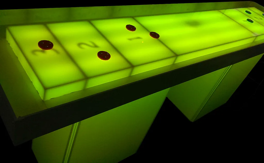 Glow shuffleboard table lit green with pucks on the board